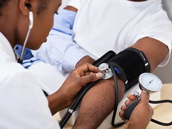 a female doctor of color taking the blood pressure of a male patient