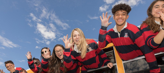 several teenagers wearing matching striped shirts leaning out of a bus window and smiling