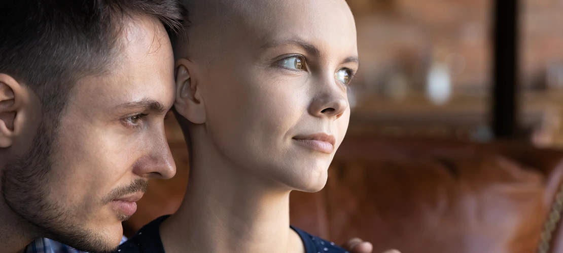 Man embracing and comforting woman who appears to be dealing with cancer or hair loss, showing intimate support and care