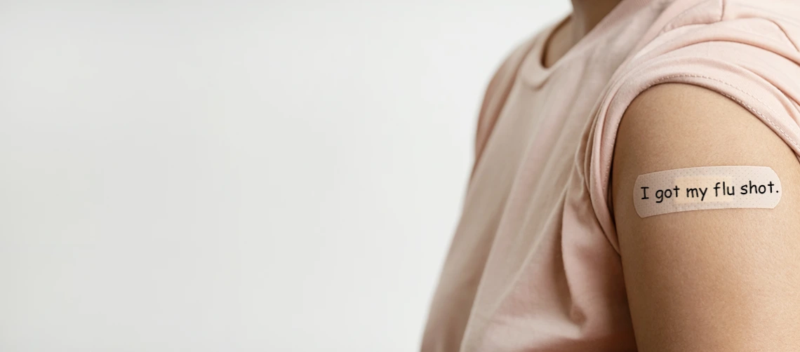 Person wearing a pink shirt with a bandage on their upper arm that reads “I got my flu shot,” symbolizing flu vaccination awareness.
